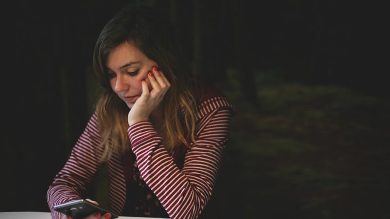 スマートフォンの画面を見ながら考え込む女性